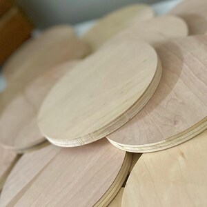 May include: A pile of unfinished, pale wooden circles, likely for crafts or DIY projects. The wood grain is visible, and the edges are smooth. The circles are stacked and arranged, creating a layered effect.