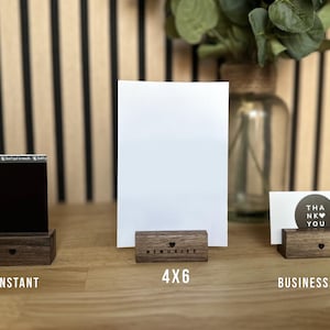 Puede incluir: Tres soportes de marco de fotos de madera de diferentes tama&ntilde;os. Los soportes son de madera oscura y tienen un recorte en forma de coraz&oacute;n en la parte delantera. Los soportes est&aacute;n etiquetados como "Instant&aacute;neo", "4x6" y "Tarjeta de visita".