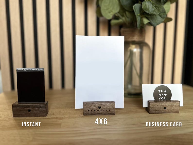 Puede incluir: Tres soportes de marco de fotos de madera de diferentes tama&ntilde;os. Los soportes son de madera oscura y tienen un recorte en forma de coraz&oacute;n en la parte delantera. Los soportes est&aacute;n etiquetados como "Instant&aacute;neo", "4x6" y "Tarjeta de visita".