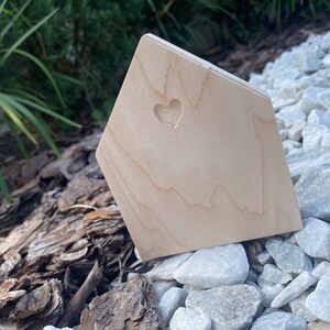 May include: A small wooden house shaped object with a heart cutout. The object is sitting on a bed of white rocks.
