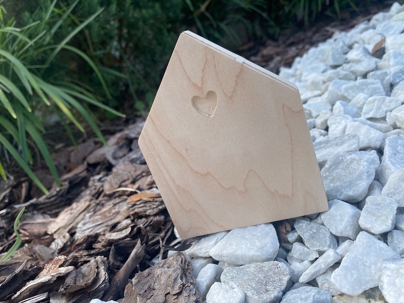 May include: A small wooden house shaped object with a heart cutout. The object is sitting on a bed of white rocks.