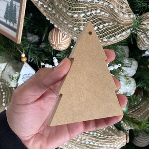May include: A brown wooden Christmas tree bauble with a hole at the top for hanging. The bauble is blank and ready to be decorated.