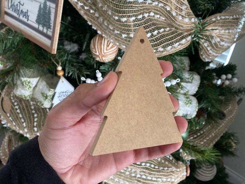 May include: A brown wooden Christmas tree bauble with a hole at the top for hanging. The bauble is blank and ready to be decorated.