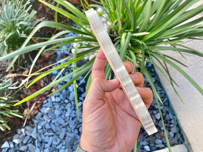 Pode incluir: Uma pilha de t&aacute;buas finas de madeira com acabamento em madeira natural. As t&aacute;buas s&atilde;o mantidas juntas por um adesivo branco fino.