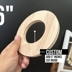 May include: A 6-inch round wooden disc with a 3-inch hole cut out in the center. The disc is light brown in color and has a smooth surface. The text "CUSTOM ADD 3" INCHES CUT INSIDE" is printed on a white label below the disc.
