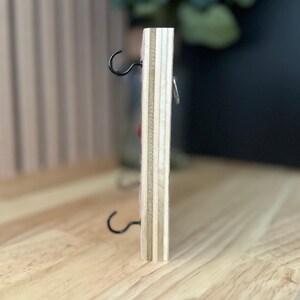 May include: A wooden wall-mounted key holder with two metal hooks and a small metal ring. The key holder is made of light wood with a natural finish.