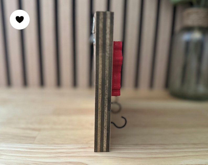 K&ouml;nnte beinhalten: Ein Wand-Schl&uuml;sselhalter aus Holz mit einem roten Blumendesign und zwei Metallhaken.