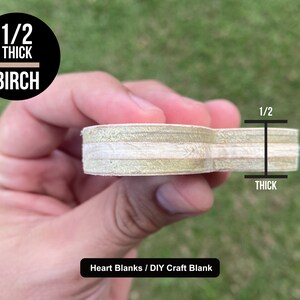 May include: A heart-shaped wooden craft blank made from birch plywood, measuring 1/2 inch thick. The blank is held in a hand, showing the wood grain and layers of plywood. The text "Heart Blanks / DIY Craft Blank" is visible below the blank.