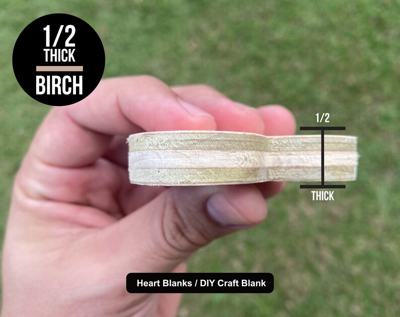 May include: A heart-shaped wooden craft blank made from birch plywood, measuring 1/2 inch thick. The blank is held in a hand, showing the wood grain and layers of plywood. The text "Heart Blanks / DIY Craft Blank" is visible below the blank.