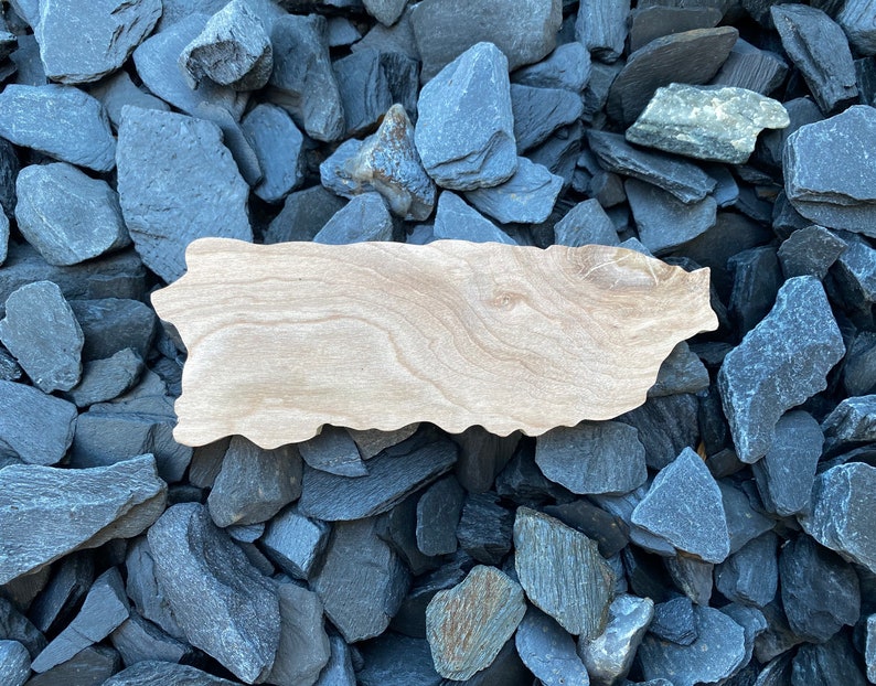 May include: A wooden cutout of the island of Puerto Rico, resting on a bed of dark gray slate stones.