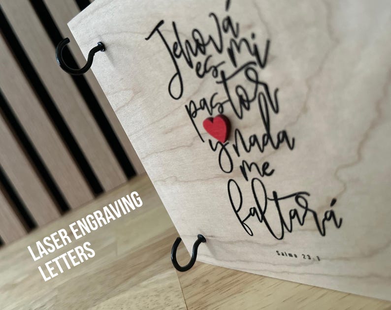May include: Laser engraved wooden plaque with the text "Jehov&aacute; es mi pastor y nada me faltar&aacute;" in black cursive lettering. A small red heart is attached to the plaque. The text "Salmo 23:1" is also engraved on the plaque.