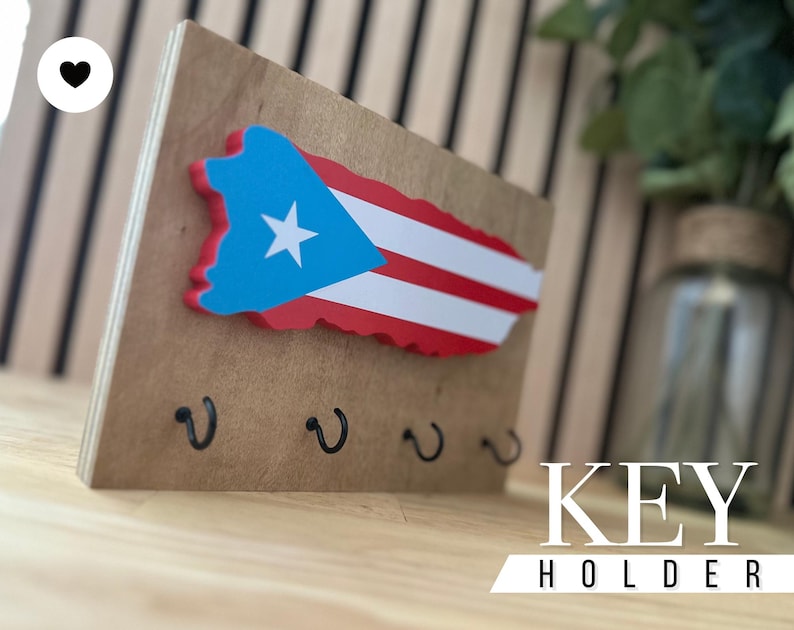 K&ouml;nnte beinhalten: Schl&uuml;sselhalter aus Holz in Form der Insel Puerto Rico mit der Flagge von Puerto Rico darauf bemalt. Der Schl&uuml;sselhalter hat vier Haken zum Aufh&auml;ngen von Schl&uuml;sseln. Der Text "KEY HOLDER" ist unter dem Schl&uuml;sselhalter aufgedruckt.