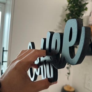 May include: Black wooden sign spelling "Coffee" in cursive. The sign is held by a hand. A decorative item for a kitchen or coffee bar. The sign is made of wood.