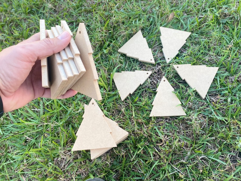 May include: A set of nine unfinished wooden Christmas tree decorations. The decorations are in the shape of a triangle and are arranged in a circle on a bed of green grass.