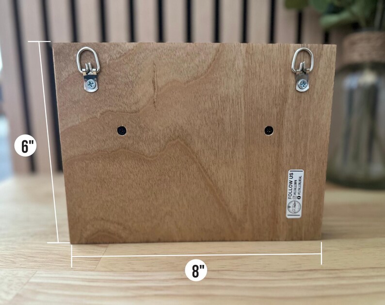 K&ouml;nnte beinhalten: Ein Holzschild mit zwei Metall-Aufh&auml;nghaken auf der R&uuml;ckseite. Das Schild ist 20,3 cm breit und 15,2 cm hoch. Das Schild hat einen kleinen Aufkleber auf der rechten unteren Ecke, auf dem "Follow Us @fireandfloral" steht.