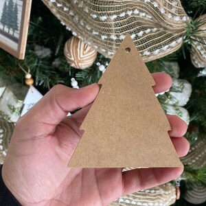May include: A brown wooden Christmas tree bauble with a hole at the top for hanging. The bauble is blank and ready to be decorated.