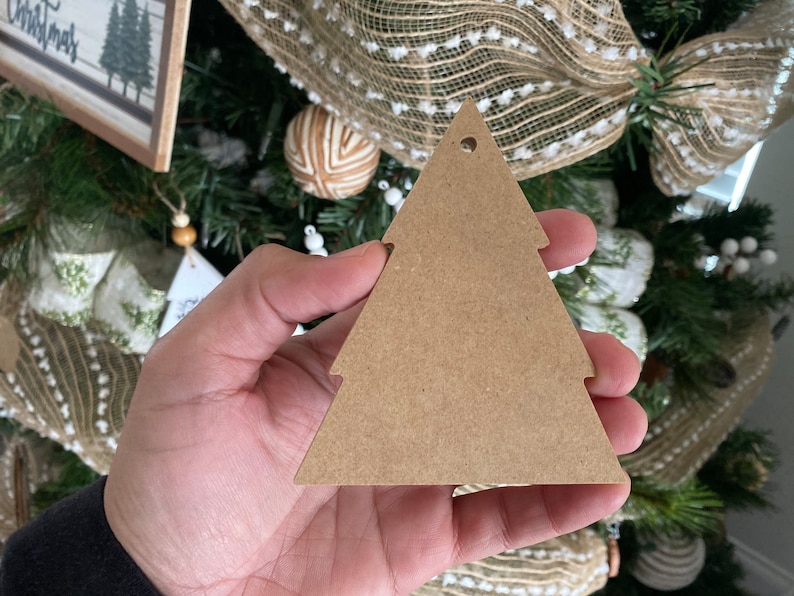 May include: A brown wooden Christmas tree bauble with a hole at the top for hanging. The bauble is blank and ready to be decorated.