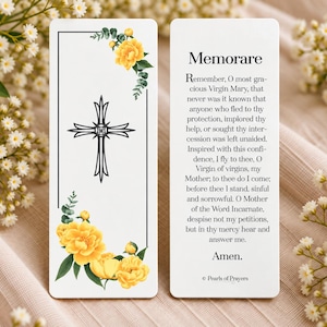 May include: A rectangular bookmark featuring a black cross centered within a thin black border, decorated with yellow flowers and green leaves at the corners. The reverse side displays the text of the Memorare prayer and the text Pearls of Prayers.
