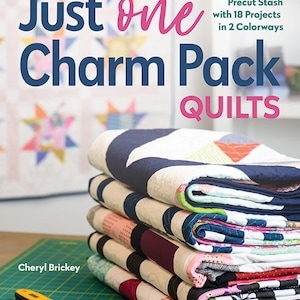 May include: A stack of colorful quilt blocks with the text "Just one Charm Pack Quilts" and "BUST Your Precut Stash with 18 Projects in 2 Colorways" on the cover of a book titled "Just one Charm Pack Quilts".