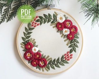Peut inclure: Un cercle de broderie blanc avec un motif de couronne florale rouge et blanche. La couronne est composée de fleurs rouges et blanches avec des feuilles vertes. Le texte "PDF PATTERN" est dans un cercle vert en haut à gauche du cercle.
