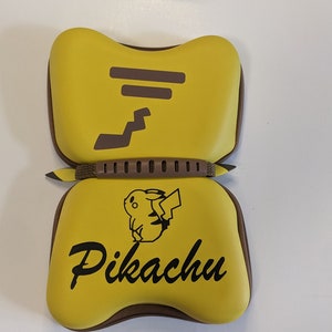 Puede incluir: Estuche de transporte amarillo y marr&oacute;n para Nintendo Switch con un dise&ntilde;o de Pikachu. El estuche tiene una cremallera y un asa.