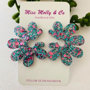 May include: Flower-shaped earrings with teal, pink, and silver glitter. The earrings are displayed on a white card with the text "Miss Molly & Co Jewellery & Gifts" and "Follow us on Facebook".