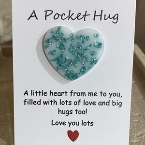 May include: A white card with a teal heart-shaped resin piece with glitter embedded in it. The card reads "A Pocket Hug" and "A little heart from me to you, filled with lots of love and big hugs too! Love you lots".