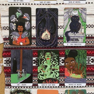 Pode incluir: Uma coleção de doze cartas de tarô dispostas em quatro fileiras, apresentando diversas ilustrações, incluindo uma árvore, um gato, uma bicicleta e várias figuras. Cada carta exibe um título único como Ace of Oaks, Seer of Moths, Death e Justice.