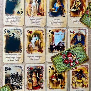 Könnte beinhalten: Ein Satz Spielkarten im Vintage-Stil mit aufwendigen Bordüren und Illustrationen. Jede Karte zeigt ein einzigartiges Bild, eine Nummer und ein Symbol. Die Karten liegen auf einer Holzoberfläche, mit einer dekorativen Karte mit Rosen.