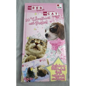May include: A pink rectangular box containing 34 Valentines with Poster, featuring images of a kitten and a puppy wearing tiaras. The text reads The Dog Princess, The Cat Princess, 34 Valentines with Poster, and Includes 34 Fold & Seal Cards.