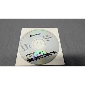 May include: A silver Microsoft Encarta Encyclopedia 2000 CD-ROM disc featuring black text that reads Microsoft, Encyclopedia Disc, and The #1 Name in Multimedia Encyclopedias. The disc includes warnings about illegal copies and distribution.