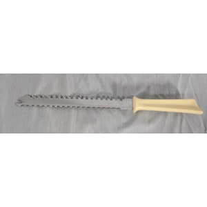 May include: A serrated knife featuring a long, metallic blade with a distinct notched tip and a smooth, cream-colored plastic handle. The blade has a uniform row of small teeth along the edge, designed for cutting, with a sturdy, ergonomic grip.