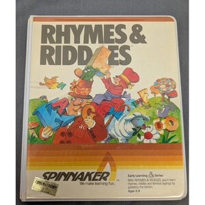 Peut inclure: Une boîte de jeu vidéo rectangulaire pour Rhymes & Riddles de Spinnaker, avec une illustration colorée de personnages, de lettres et d'un mouton. La couverture inclut le titre, le logo Spinnaker et le texte Early Learning Series, Ages 5-9.