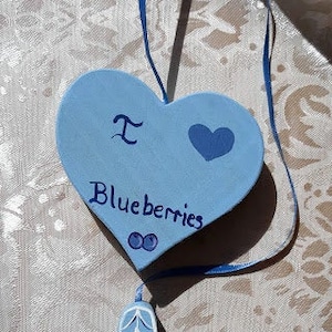 May include: A blue heart-shaped wooden ornament with the text "I love blueberries" and a small blue heart. A blue wooden basket with a white handle and blue blueberries is hanging from the heart.