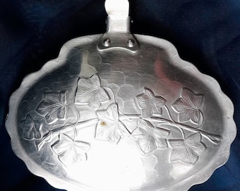 May include: A silver serving dish with a handle and a design of ivy leaves. The dish is made of aluminum and has a hammered finish.