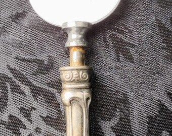 May include: A silver cheese knife with an ornate handle. The blade is oval shaped and the handle is decorated with a floral design.