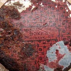 May include: A rusty, red, and white metal lid with the text "MRS. BOX'S, BROOKLYN, N.Y." printed on it. The lid has a faded, patterned design.