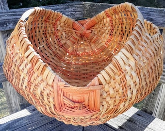 May include: A large, woven basket with a heart shape. The basket is made of natural materials and has a light brown and orange color.