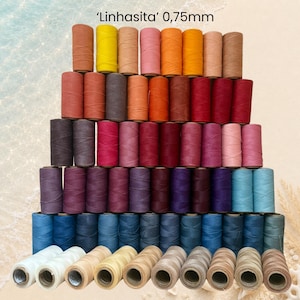 Könnte beinhalten: Eine Sammlung von Linhasita 0,75 mm Garnrollen, die in einer Pyramidenform angeordnet sind. Die Rollen zeigen ein breites Farbspektrum, darunter Gelb-, Orange-, Rot-, Rosa-, Lila-, Blau-, Braun- und Weißtöne, mit dem Text Linhasita 0,75 mm oben.