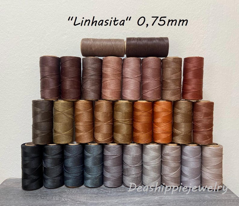 May include: A collection of Linhasita 0.75mm waxed polyester thread spools arranged in a pyramid. The spools feature a wide spectrum of neutral, brown, and grey tones, ranging from deep black and dark charcoal to light beige, tan, and warm terracotta.