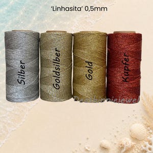 Könnte beinhalten: Vier Spulen Linhasita-Garn in 0,5 mm Stärke in den metallischen Farben Silber, Goldsilber, Gold und Kupfer. Jede Spule ist mit ihrem Farbnamen in schwarzer Schrift beschriftet, und oben im Bild steht der Text 'Linhasita' 0,5 mm.