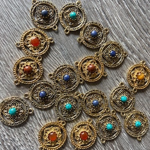 Puede incluir: Una colección de 18 dijes de metal dorado con diseños intrincados y piedras preciosas de colores. Cada dije presenta una piedra preciosa diferente, incluyendo turquesa, lapislázuli y cornalina.