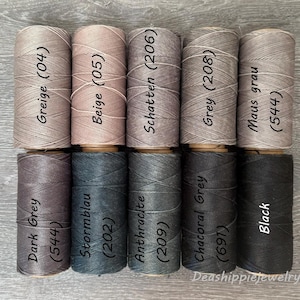 May include: Ten cylindrical spools of thread arranged in two rows of five. The top row features shades of Greige (04), Beige (05), Schatten (206), Grey (208), and Maus grau (544). The bottom row includes Dark Grey (544), Stormblau (202), Anthracite (209), Chacoral Grey (691), and Black.