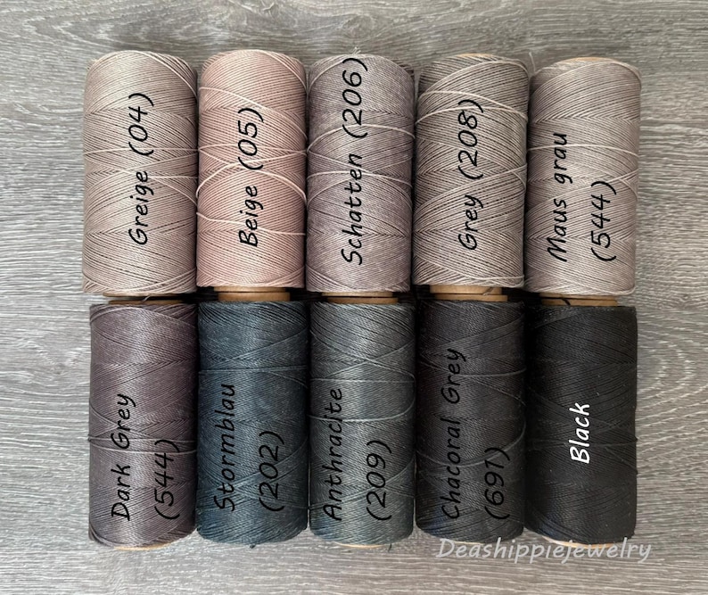 May include: Ten cylindrical spools of thread arranged in two rows of five. The top row features shades of Greige (04), Beige (05), Schatten (206), Grey (208), and Maus grau (544). The bottom row includes Dark Grey (544), Stormblau (202), Anthracite (209), Chacoral Grey (691), and Black.