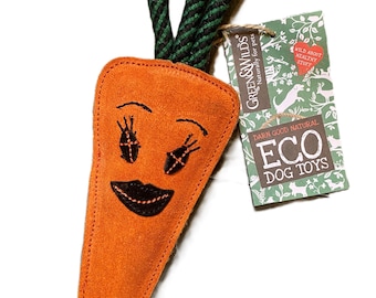 May include: Orange carrot-shaped dog toy with a stitched face and green and black rope 'carrot top'. A tag reads 'Green & Wilds' and 'Eco Dog Toys'. The toy is designed to be a fun and safe plaything for pets.