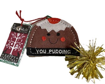 May include: A brown felt Christmas pudding cat toy with a smiling face and the text "YOU PUDDING". It has a white and red trim, a gold tinsel accent, and a tag that says "HAPPY CHRISTMAS".