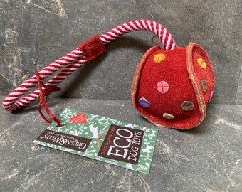 May include: A red suede dog toy with colorful stitched accents and a striped rope handle. The toy has a tag that reads "Eco Dog Toys" and "Naturally for pets".
