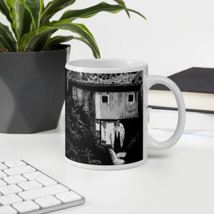 May include: White ceramic mug with a black and white illustration of a building with a window. The illustration is of a building with a window and a small roof.