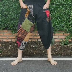 Może przedstawiać: Czarne spodnie z patchworkowym wzorem w różnych kolorach i wzorach. Spodnie mają elastyczny pas i kieszenie.