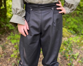Puede incluir: Un pantalón negro de rodilla con cierre de botón y cintura alta. El pantalón tiene un frente plisado y está hecho de una tela gruesa y texturizada.